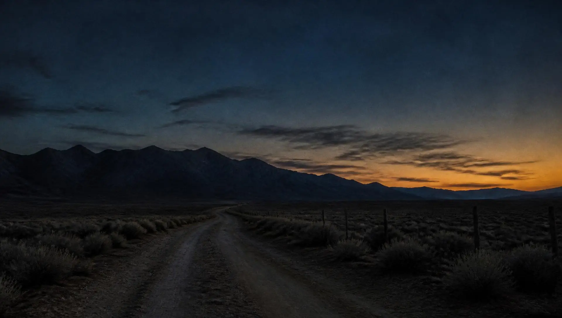 Dirt road running toward a dark mountain ridge at dusk